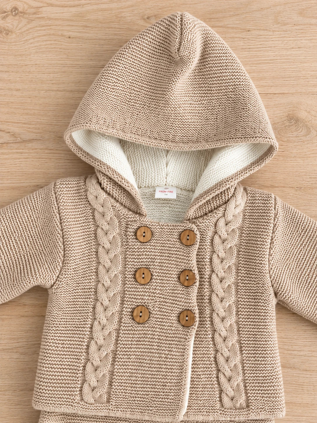 Detalle de chaqueta de punto para bebé con capucha, trenzas y botones